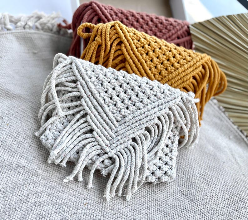 Macrame handwoven purses in a row one behind another-beige, mustard yellow, brownz Placed upright on plain beige fabric.