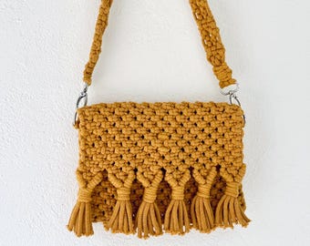 May include: A mustard yellow crocheted crossbody bag with a long strap and fringe detail.
