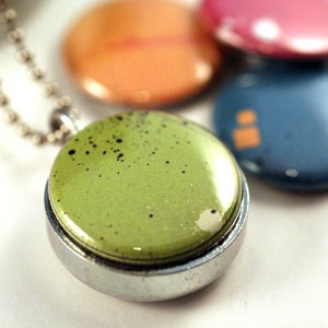 May include: A silver chain necklace with a green pendant. The pendant is round and has a shiny, speckled finish.