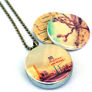May include: A silver locket necklace with a brass chain. The locket has two interchangeable images. One image is a vintage postcard of a Joshua Tree in the desert. The other image is a vintage postcard of the "Welcome to Las Vegas" sign.