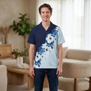 May include: A short-sleeved button-down shirt featuring a colour-blocked design that transitions from dark navy blue on the left to light blue on the right, accented by a diagonal pattern of white hibiscus flowers and dark blue tropical leaves.