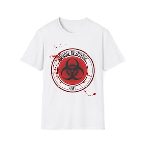 Könnte beinhalten: Weißes T-Shirt mit roter und schwarzer Grafik. Das Design zeigt ein Biohazard-Symbol in einem Kreis mit dem Text "ZOMBIE RESPONSE UNIT". Rote Spritzer ergänzen das Design.