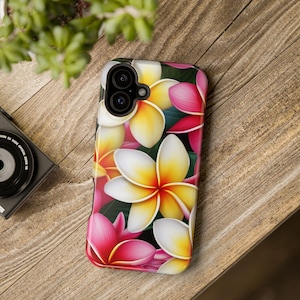 May include: A phone case featuring a vibrant floral design with pink, yellow, and white plumeria flowers. The case has a glossy finish and a black camera cutout. The background is a wooden surface.