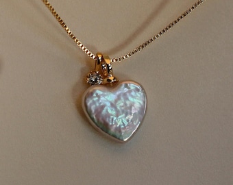 May include: A gold chain necklace with a heart-shaped pendant. The pendant is made of white mother-of-pearl and has a small diamond accent.