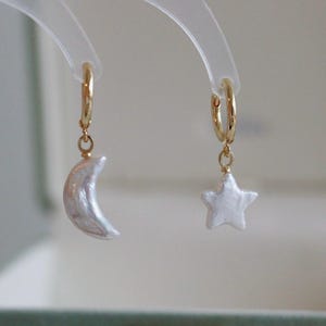 May include: A pair of gold hoop earrings with a pearl crescent moon charm on one earring and a pearl star charm on the other earring.
