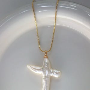 May include: A gold chain necklace with a white baroque pearl cross pendant.