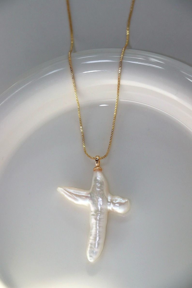 May include: A gold chain necklace with a white baroque pearl cross pendant.