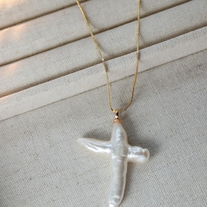 May include: A gold chain necklace with a white pearl cross pendant.