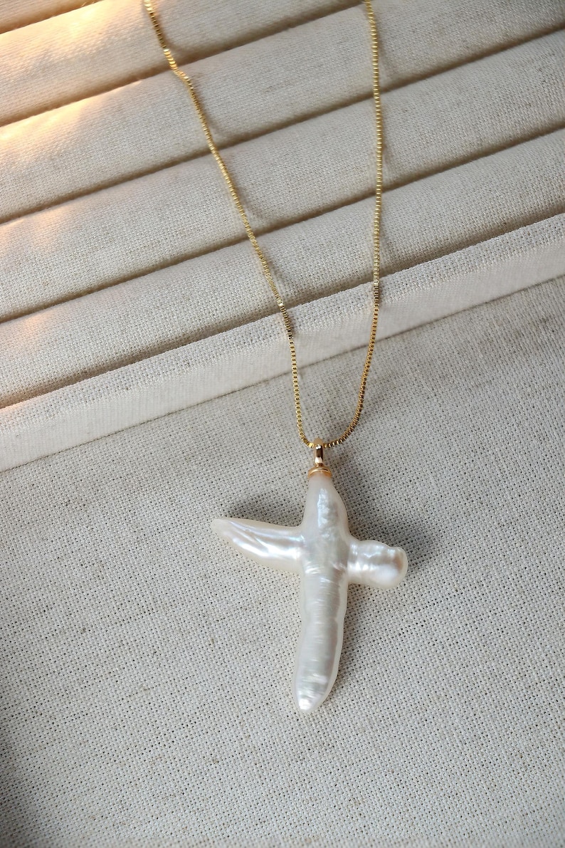 May include: A gold chain necklace with a white pearl cross pendant.