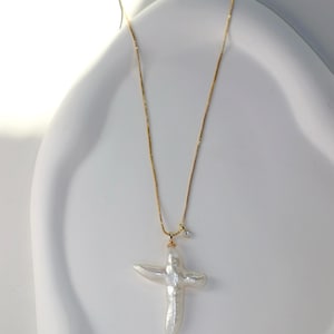 May include: A gold chain necklace with a large white pearl cross pendant and a small diamond accent.