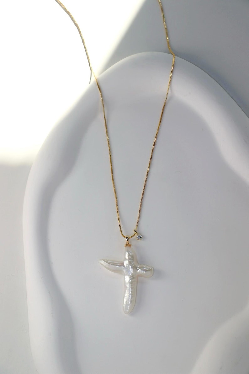 May include: A gold chain necklace with a large white pearl cross pendant and a small diamond accent.