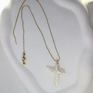 May include: A gold chain necklace with a white baroque pearl cross pendant.