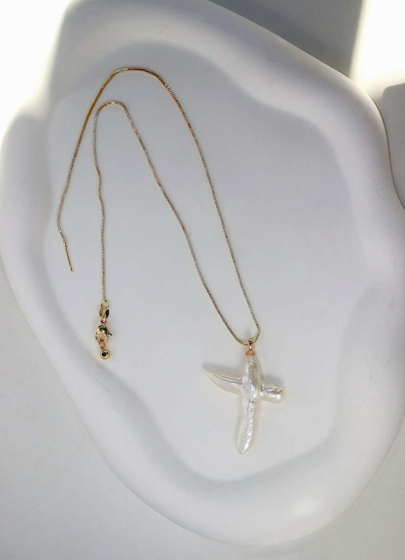 May include: A gold chain necklace with a white baroque pearl cross pendant.