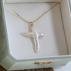 May include: A white pearl cross pendant necklace on a gold chain in a green velvet jewellery box.