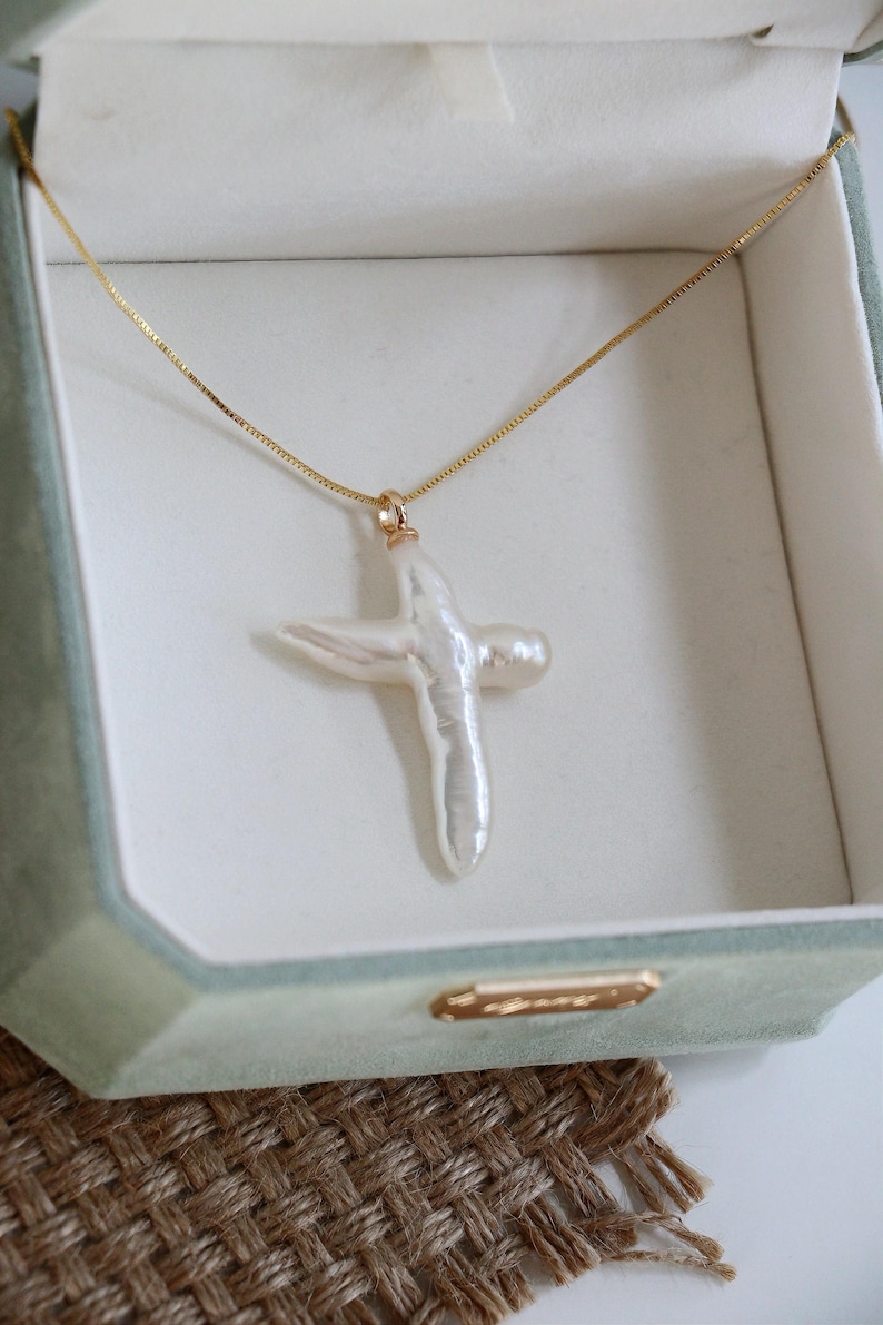 May include: A white pearl cross pendant necklace on a gold chain in a green velvet jewellery box.
