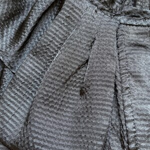 May include: Close-up of a dark gray fabric with a subtle striped pattern. The fabric appears to be textured, with visible seams and folds. The image highlights the details of the material, showcasing its weave and construction.