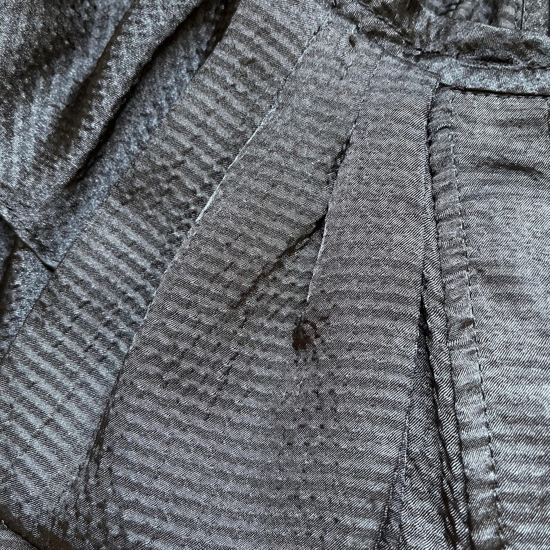 May include: Close-up of a dark gray fabric with a subtle striped pattern. The fabric appears to be textured, with visible seams and folds. The image highlights the details of the material, showcasing its weave and construction.
