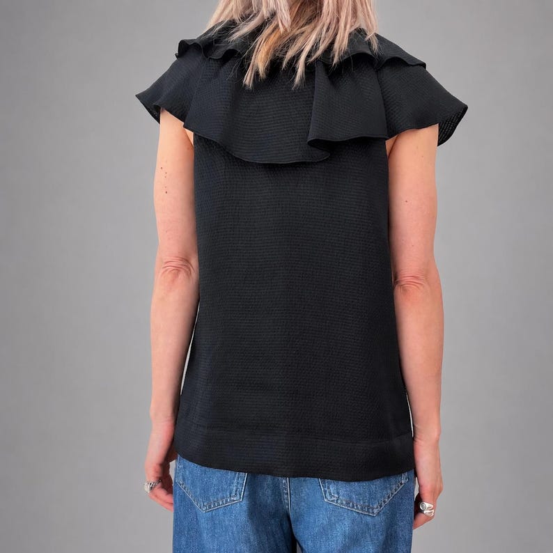 May include: Black sleeveless top with a ruffled neckline and cap sleeves. The top has a textured fabric and a straight hemline. The model is wearing blue jeans. The top is a stylish addition to any wardrobe.
