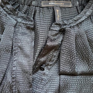 May include: Close-up of a black blouse with a textured pattern and a mandarin collar. The blouse has a button closure and a label that reads "BCBGMAXAZRIA". The fabric has a subtle sheen.