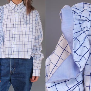May include: White button-down shirt with a blue grid pattern. The shirt has long sleeves and a cropped fit. The sleeves feature a unique ruffled design. The shirt is paired with blue jeans.