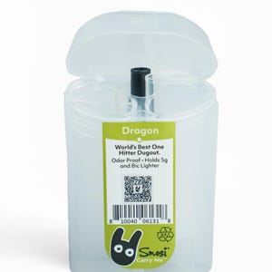 Puede incluir: Un recipiente de plástico transparente con tapa abatible, etiquetado como "Dragon". El recipiente contiene un objeto negro y presenta una etiqueta verde y blanca con texto, incluyendo "World's Best One Hitter Dugout" y un código QR. El recipiente está diseñado para contener 5g y un encendedor Bic.