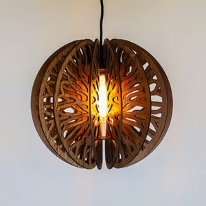 Puede incluir: Una lámpara colgante de madera con un diseño circular y geométrico. La lámpara está hecha de múltiples capas de madera, cada una con un patrón recortado. La lámpara está iluminada por una bombilla de luz blanca cálida.
