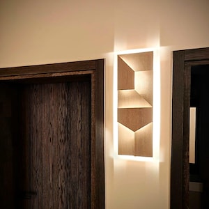Könnte beinhalten: Eine moderne Wandleuchte aus Holz mit geometrischem Design. Die Leuchte wird mit warmweißem Licht beleuchtet.