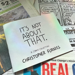 Op de afbeelding: Een comix-collectie getiteld "IT'S NOT ABOUT THAT" door Christopher Furniss. De witte cover met zwarte tekst ligt op een krant met krantenkoppen en strips.
