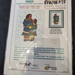 May include: A counted cross-stitch chart titled "HUGS" by Lynn Blaikie. The artwork depicts two figures embracing, with a stitch count of 120 x 163. The package includes the "Studio Art Needlework" logo and the text "Create a Masterpiece!"