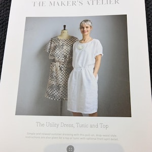May include: A sewing pattern booklet for a simple, relaxed summer dress, tunic, or top. The cover features a white dress with a drop waist and a model wearing the dress. The text on the cover reads "The Maker's Atelier" and "The Utility Dress, Tunic and Top".