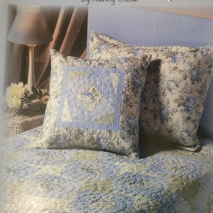 May include: A blue and white floral patterned quilt with a blue and white floral patterned pillow on top. The quilt is on a bed with a blue headboard. The title "Fast Asleep" is written on the headboard, with the author's name "by Nancy Odom" below it.
