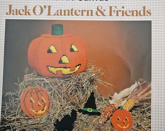May include: A plastic canvas craft kit featuring a Jack O'Lantern and friends. The kit includes patterns for a large pumpkin, a smaller pumpkin, a black cat, and a witch's hat. The image shows the finished crafts on a bed of straw with candy corn scattered around.