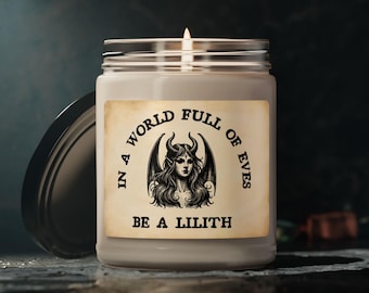 May include: A clear glass jar candle with a white wax fill and a lit wick. The label features a vintage-style paper background with a black illustration of a horned, winged figure and the text: IN A WORLD FULL OF EVES BE A LILITH.