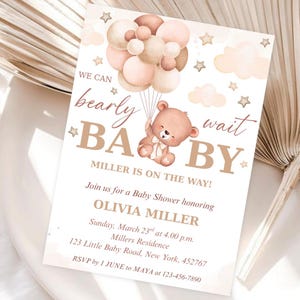 Può includere: Invito per baby shower con un orsetto che tiene dei palloncini. Il testo sull'invito recita "We can bearly wait BABY" e fornisce i dettagli per il baby shower di Olivia Miller, tra cui data, ora e luogo.
