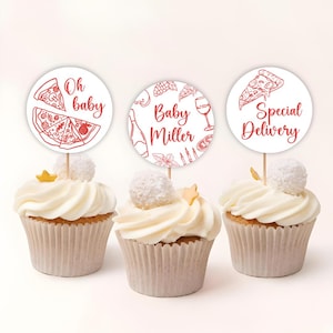 May include: Three cupcakes with white frosting, each topped with a round paper topper on a wooden stick. The toppers have red illustrations and text: "Oh baby", "Baby Miller", and "Special Delivery". Each cupcake has a white candy ball and a gold star.