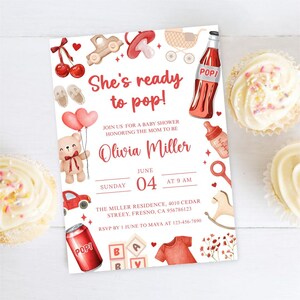 May include: Baby shower invitation with the text "She's ready to pop!" in red script. The invitation features illustrations of baby-related items like a teddy bear, baby bottle, and a red soda bottle. Two cupcakes are on the sides.