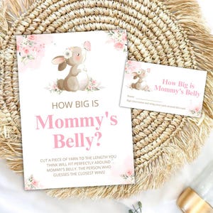 May include: A baby shower game set featuring a bunny illustration with floral accents. The main card reads "How Big is Mommy's Belly?" in pink text, with instructions below. A smaller card repeats the title and has a space for a name.