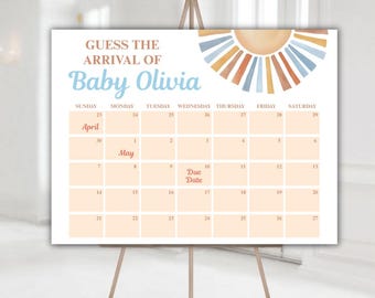May include: A baby shower sign on an easel. The sign features a calendar design with the text "Guess the Arrival of Baby Olivia." The calendar highlights April and May dates, with a sun graphic in the upper right corner.