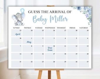 Op de afbeelding: Een babyshowerkalender met de tekst "Raad de aankomst van Baby Miller". De kalender toont een blauwe olifant met een ballon, bloemaccenten en een kalenderraster met de vervaldatum gemarkeerd. De kalender wordt weergegeven op een houten ezel.