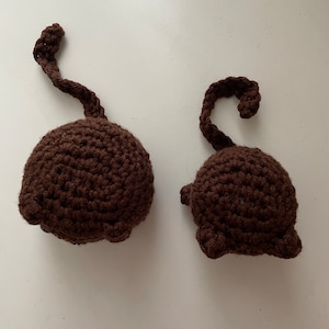 May include: Two brown crocheted monkey plushies with long tails. The plushies are sitting on a white surface.