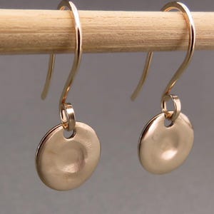 May include: A pair of gold-toned dangle earrings with a round disc shape. The discs have a hammered texture and a small hole in the center.