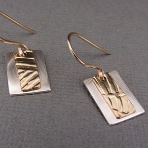 May include: A pair of silver earrings with gold rectangular accents. The gold accents have a textured pattern.