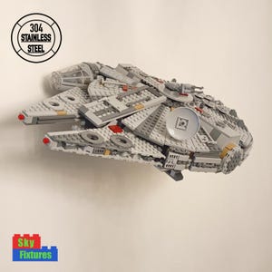 May include: A grey and white Lego Millennium Falcon spaceship model with red and yellow accents. The model is built and ready to display.