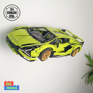 May include: A lime green toy sports car with gold-coloured wheels. The car is made of interlocking blocks and has a detailed interior. A circular logo above the car reads "304 STAINLESS STEEL". The car is mounted on a white wall.