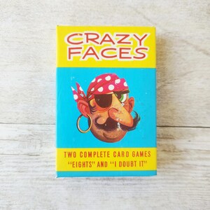 May include: A boxed card game titled "CRAZY FACES" with a cartoon pirate illustration. The box is yellow and turquoise with the text "TWO COMPLETE CARD GAMES 'EIGHTS' AND 'I DOUBT IT'". The pirate has a red and white polka dot bandana, an eye patch, and a large mustache.