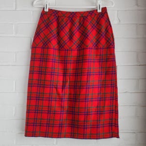 May include: A knee-length skirt featuring a vibrant red base with a prominent plaid pattern in shades of blue and green. The garment has a high-waisted design with a straight silhouette and is displayed on a white plastic hanger for presentation.