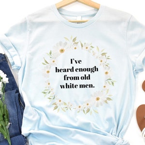 May include: Light blue t-shirt with a white floral wreath design and the text "I've heard enough from old white men."