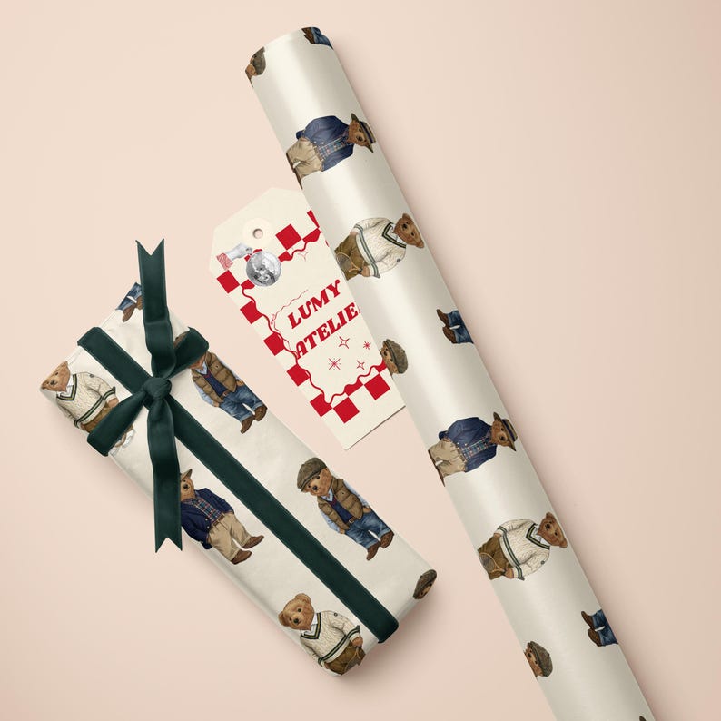 May include: Gift wrap featuring a repeating pattern of teddy bears in various outfits. A wrapped gift with a dark green ribbon and a tag with the text "LUMY ATELIE" are also visible. The background is a light pink.
