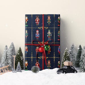 May include: A wrapped gift with navy blue paper featuring a pattern of colorful nutcracker soldiers. The gift is tied with a red ribbon and adorned with a red and green ornament. Miniature Christmas trees and a toy car are in the foreground.