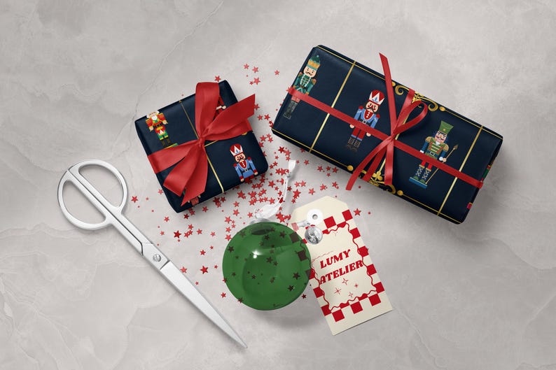 May include: Two wrapped gifts with red bows and nutcracker-themed paper, a green ornament, scissors, and a tag that says "LUMY ATELIER" with a red and white checkered border. Red star confetti is scattered around the items.